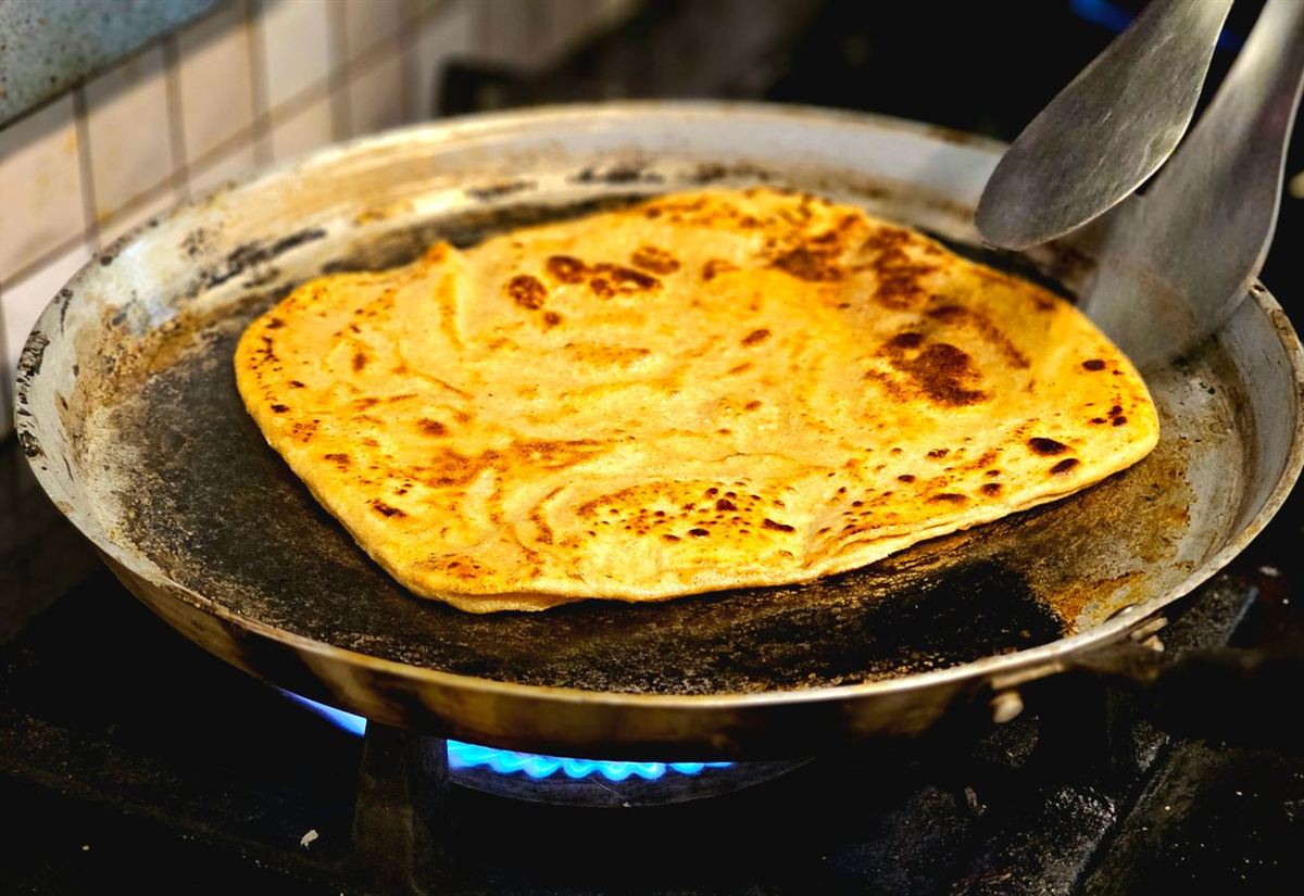 A paratha cooking on a hot tawa over a gas flame