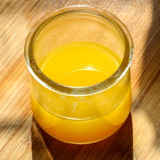A sealed glass jar of golden ghee on a wooden board